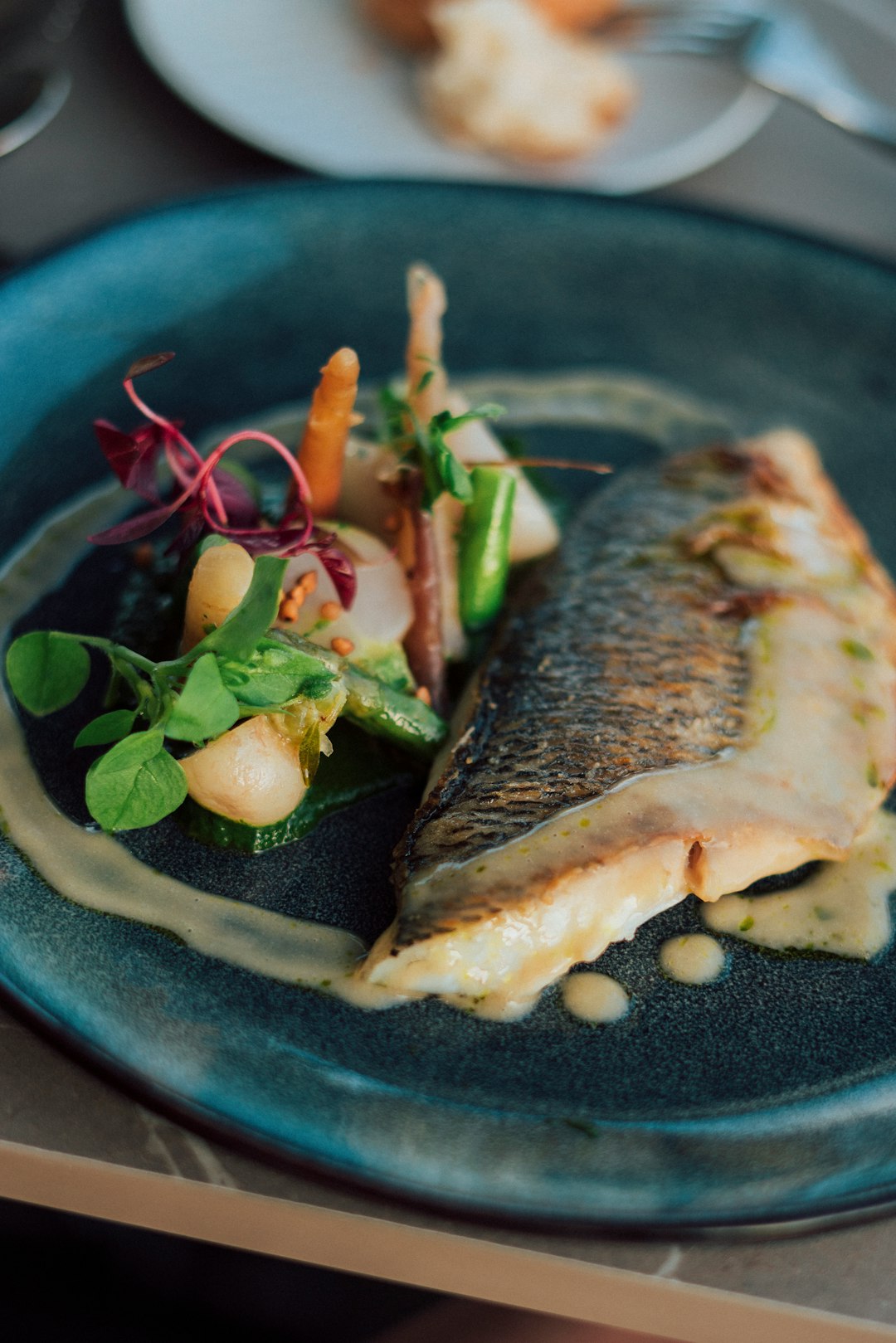 a-blue-plate-topped-with-a-piece-of-fish-next-to-a-salad-epmw1k6zmhu